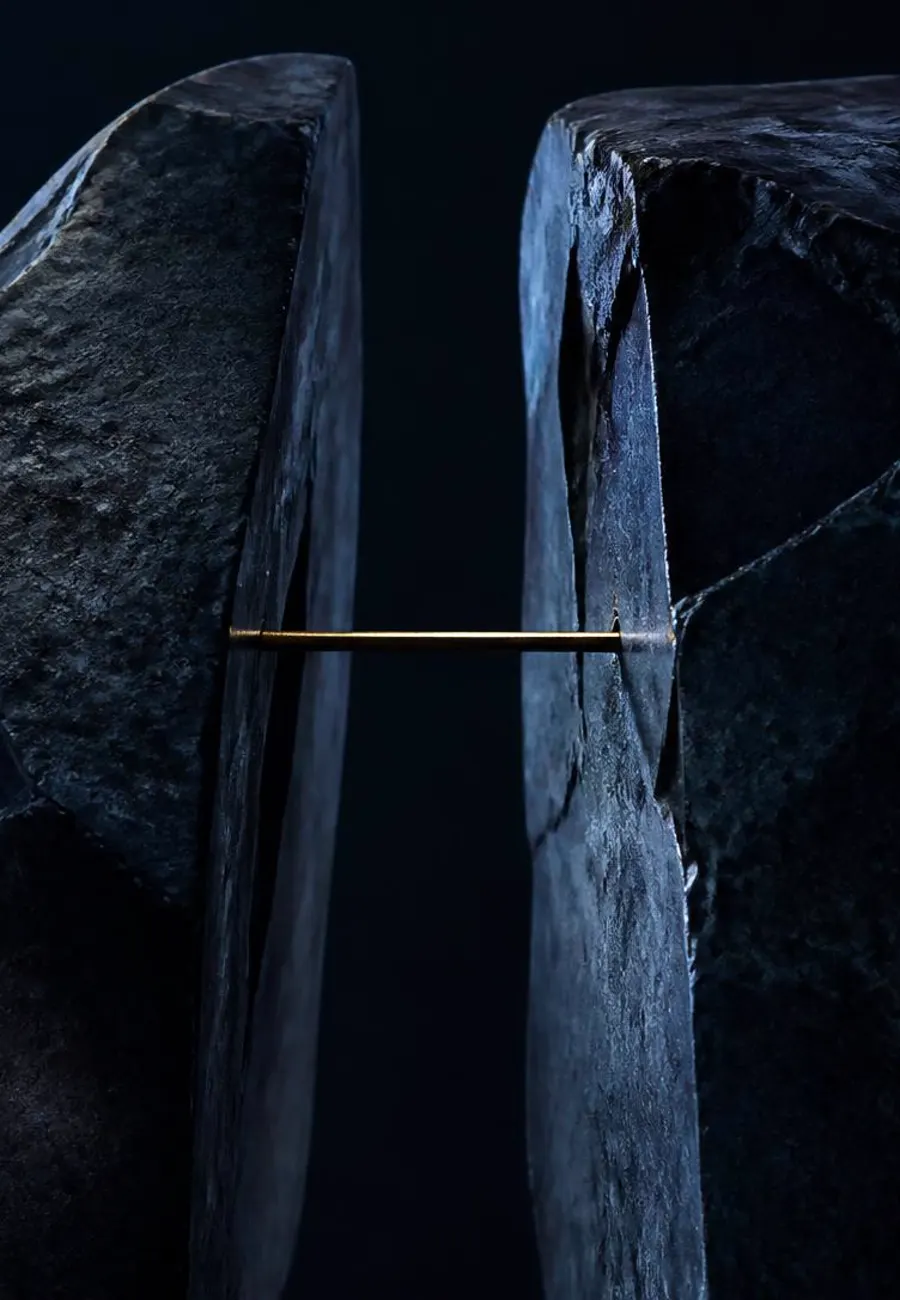 Two split halves of dark stone held apart by a single thin brass rod